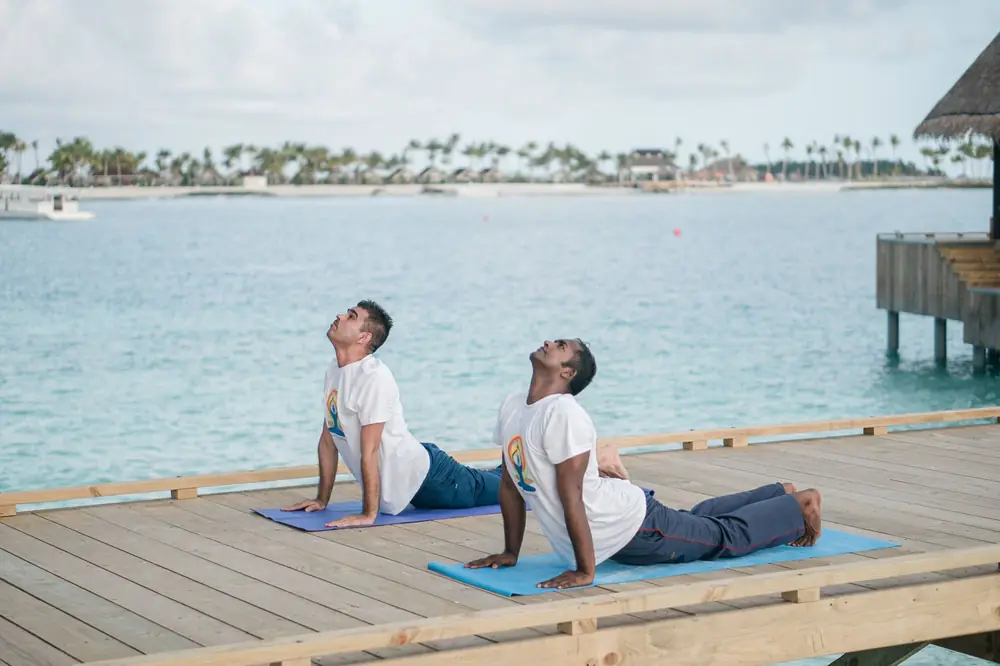 Two people practicing yoga on an oceanfront deck